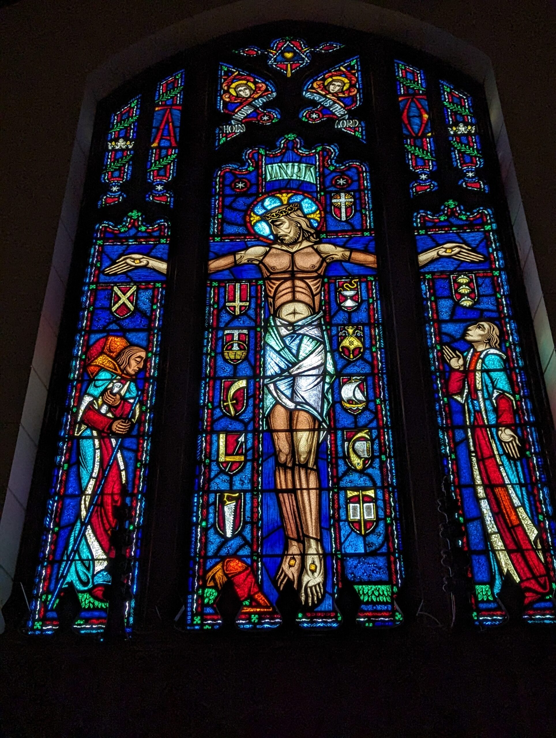 Stained glass above the high altar featuring the Pilgrim, burdened with the weight of the world, laying his cares before the cross and then giving thanks and praise for the freedom that comes through Christ. 